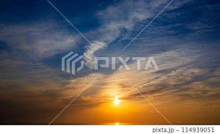 夕暮れの空に沈む夕陽と流れゆく雲 114939051