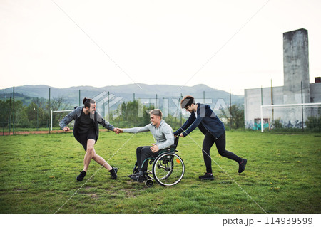 Young man in wheelchair spending free time outdoor with friends, having fun in city. Male friendship. 114939599