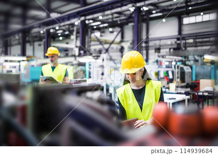 Warehouse employees in warehouse. Two workers in reflective clothing in modern industrial factory, heavy industry, manufactrury. 114939684
