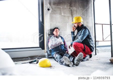 Colleague calling ambulance and giving first aid to injured worker, in pain after accident at construction site Concept of occupational safety and health in workplace. 114939793