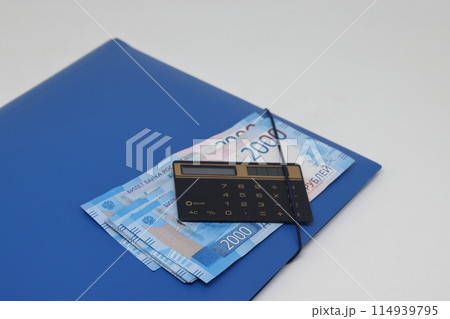 Calculator and banknotes lie on a folder for papers, financial accounting and control. Calculator and banknotes lie on a folder for papers, financial accounting and control. 114939795
