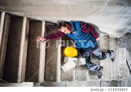 Male worker lying on the stairs after fall. Work injury, accident in workplace. Male worker lying on the stairs after fall. Work injury, accident in workplace. 114939803