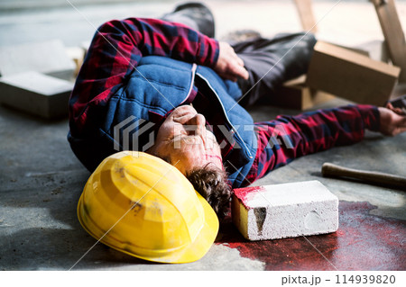 An unconscious man worker lying on the floor after a head injury. Work injury, accident in workplace. An unconscious man worker lying on the floor after a head injury. Work injury, accident in workplace. 114939820