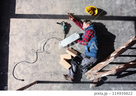 Male worker lying on the floor after fall from ladder, holding his knee. Work injury, accident in workplace. 114939822