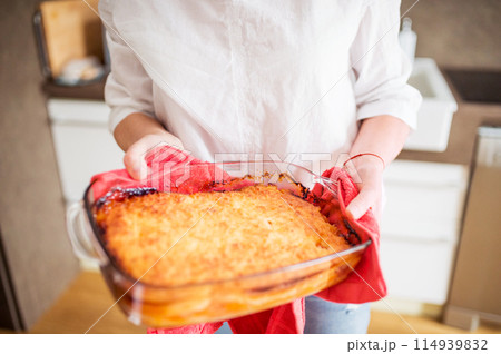Mature woman preparing homemade lasagna, holding hot glass baking dish. 114939832