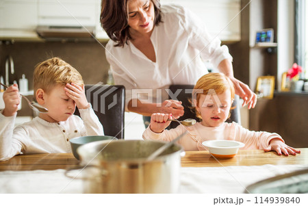 Grandma takes care of the grandchildren while their parents are at work, serving lunch to kids, putting soup in plate. 114939840