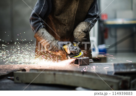 Close up of work of welder in workshop, operating welding machine, wearing protective clothing and a welding mask. Close up of work of welder in workshop, operating welding machine, wearing protective clothing and a welding mask. 114939883