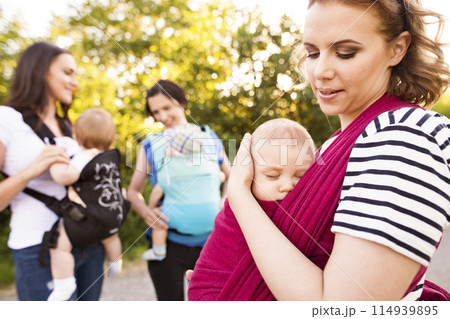 Mothers carrying babies in carriers, slings or wraps. Babywearing. Mothers carrying babies in carriers, slings or wraps. Babywearing. 114939895