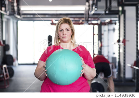 Portrait of overweight woman exercising in gym, holding medicine ball 114939930