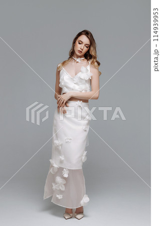 A woman in a white dress with flowers on it poses for a photo A woman in a white dress with flowers on it poses for a photo 114939953