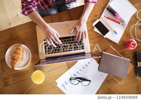 Top view on desk of university student is writing her thesis on a laptop, sitting at home on the couch. 114939989