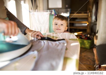 Son looking at mother ironing. Family doing household chores. 114940182