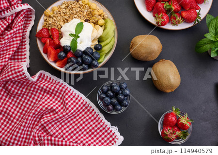 Healthy breakfast. Granola with strawberries, kiwi, banana and blueberries in a round plate on a black table. Healthy and tasty food 114940579