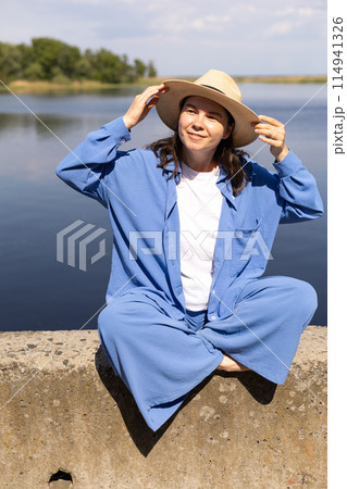 young woman in a straw hat sits on the seashore and smiles young woman in a straw hat sits on the seashore and smiles 114941326