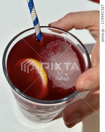 Holding glass of red sangria, Tinto de Verano, top view on white table Holding glass of red sangria, Tinto de Verano, top view on white table 114941387