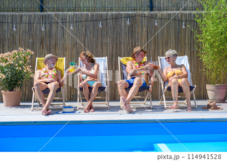 Group of cheerful seniors lying on lounge chairs by swimming pool and sunbathing. Spending hot day outdoors in backyard. Group of cheerful seniors lying on lounge chairs by swimming pool and sunbathing. Spending hot day outdoors in backyard. 114941528