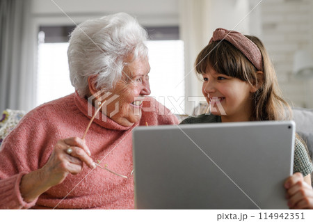 Grandmother with cute girl scrolling on tablet, girl teaching senior woman to work with technology, internet. Portrait of elderly woman spending time with granddaughter. Grandmother with cute girl scrolling on tablet, girl teaching senior woman to work with technology, internet. Portrait of elderly woman spending time with granddaughter. 114942351