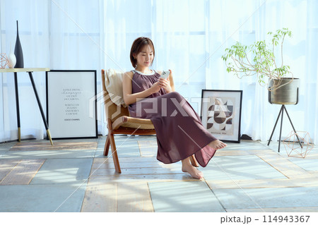 部屋の中で椅子に座ってスマホを見る女性 114943367