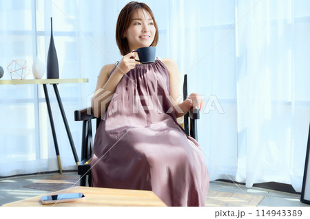 部屋の中で椅子に座ってコーヒーを飲む女性 部屋の中で椅子に座ってコーヒーを飲む女性 114943389
