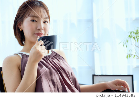 部屋の中で椅子に座ってコーヒーを飲む女性 114943395