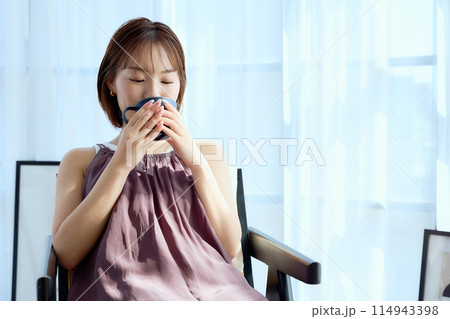 部屋の中で椅子に座ってコーヒーを飲む女性 114943398