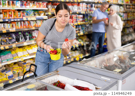 Young girl choosing frozen peppers in freezer in grocery store 114946249