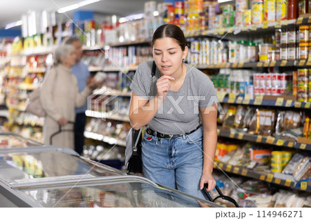 Young woman looking at products in glass refrigerator in store 114946271