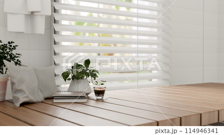 A wooden tabletop against the window, featuring potted plants, a coffee cup, books, and pillows. 114946341