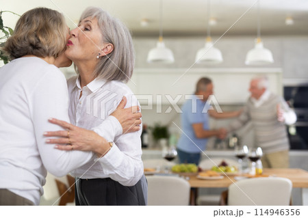 As two elderly woman meet, they exchange warm greeting by embracing with a gentle kiss on cheek As two elderly woman meet, they exchange warm greeting by embracing with a gentle kiss on cheek 114946356
