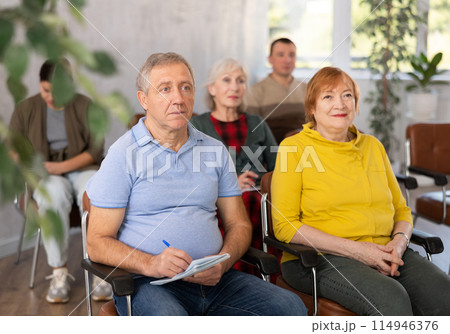 Interested aged man and woman listening to lecture in auditorium Interested aged man and woman listening to lecture in auditorium 114946376
