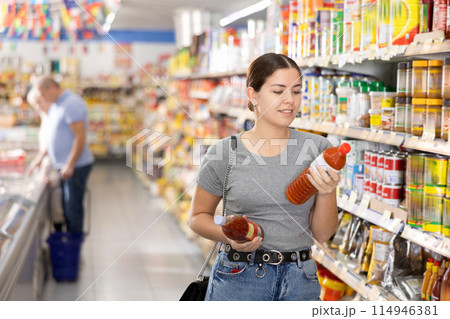 Woman choosing hot chili sauce for herself in supermarket Woman choosing hot chili sauce for herself in supermarket 114946381
