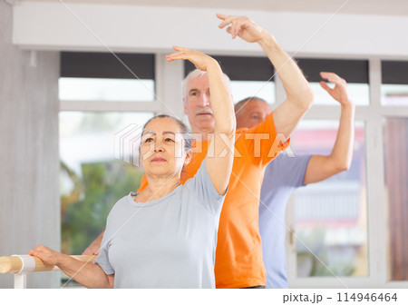 Close-up view of mature woman practicing ballet positions standing by ballet-barre Close-up view of mature woman practicing ballet positions standing by ballet-barre 114946464