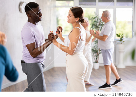 Girl teacher dances pair dance with african male student of fitness class Girl teacher dances pair dance with african male student of fitness class 114946730