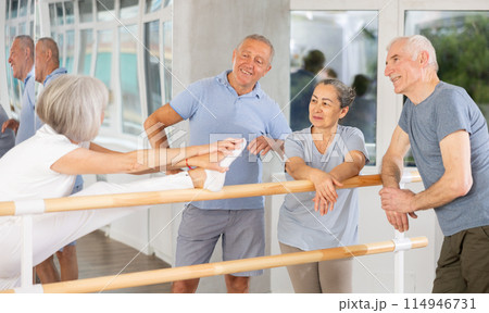 Active old attendees of ballet courses communicating cheerfully at ballet-barre Active old attendees of ballet courses communicating cheerfully at ballet-barre 114946731
