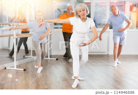Positive mature woman practicing ballet positions standing in row with others Positive mature woman practicing ballet positions standing in row with others 114946886