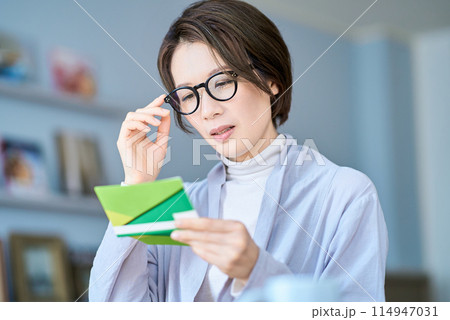 困った表情で銀行口座の通帳を見る女性 114947031