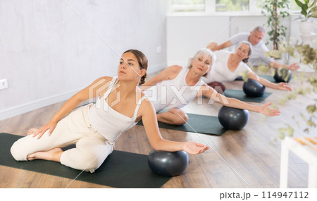 Elderly woman posing with soft ball at group class in modern yoga studio Elderly woman posing with soft ball at group class in modern yoga studio 114947112