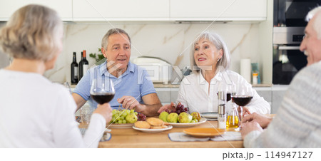 Two mature married couples are sitting at table, enjoying food and wine, chatting. 114947127