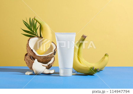 Mock up for cosmetic product advertising, which manufactured from banana and coconut, a blank label tube placed in front with coconut and banana striking in back against yellow background, copy space 114947794