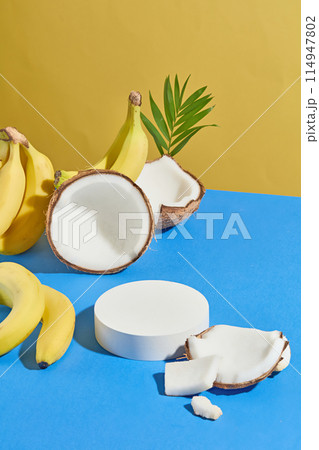 Minimalist style photo from high angle, a blank platform displayed on blue countertop with dry coconut pieces and banana bunch flat lay on. Space for displaying product or adding design elements 114947802