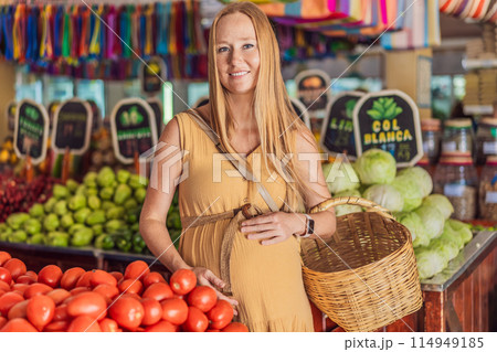 A pregnant woman is at a fruit stand in a grocery store Pregnant woman buying organic vegetables and fruits at Mexican style farmers market A pregnant woman is at a fruit stand in a grocery store Pregnant woman buying organic vegetables and fruits at Mexican style farmers market 114949185