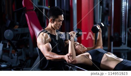 Asian trainer is introducing the use of dumbbell to a student in the gym 114951923