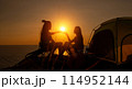 Two female hikers set up camp on a seaside cliff. 114952144