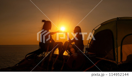 Two female hikers set up camp on a seaside cliff. 114952144