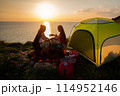 Two female hikers set up camp on a seaside cliff. 114952146