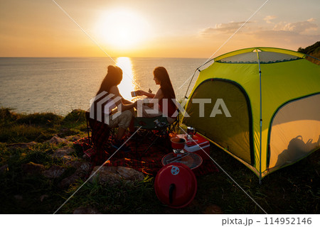 Two female hikers set up camp on a seaside cliff. 114952146