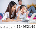Father and mother with daughter relaxing and using laptop computer on bed. 114952149