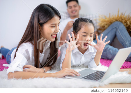 Father and mother with daughter relaxing and using laptop computer on bed. 114952149