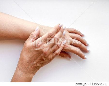 Hands middle age woman with white manicured nails gently touching each other on white background, top view. Flat lay composition. Skincare and hand care or mother love concept. Hands middle age woman with white manicured nails gently touching each other on white background, top view. Flat lay composition. Skincare and hand care or mother love concept. 114953429