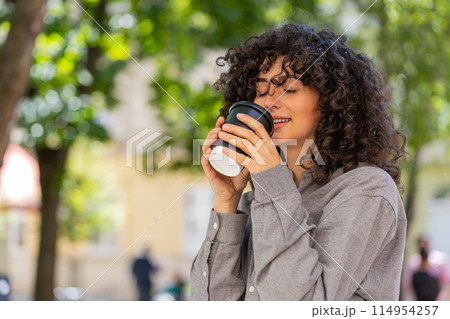 Happy young woman enjoying drinking morning coffee hot drink relaxing taking a break on city street 114954257